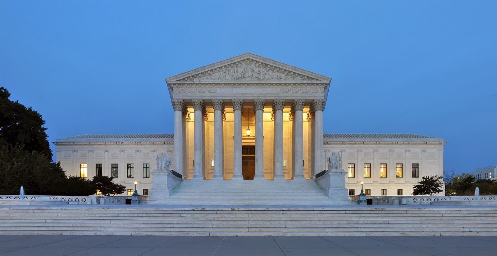 The United States Supreme Court building at dusk, columns lit from within