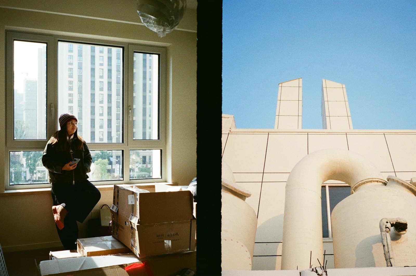 A person sitting by an apartment window beside packed moving boxes